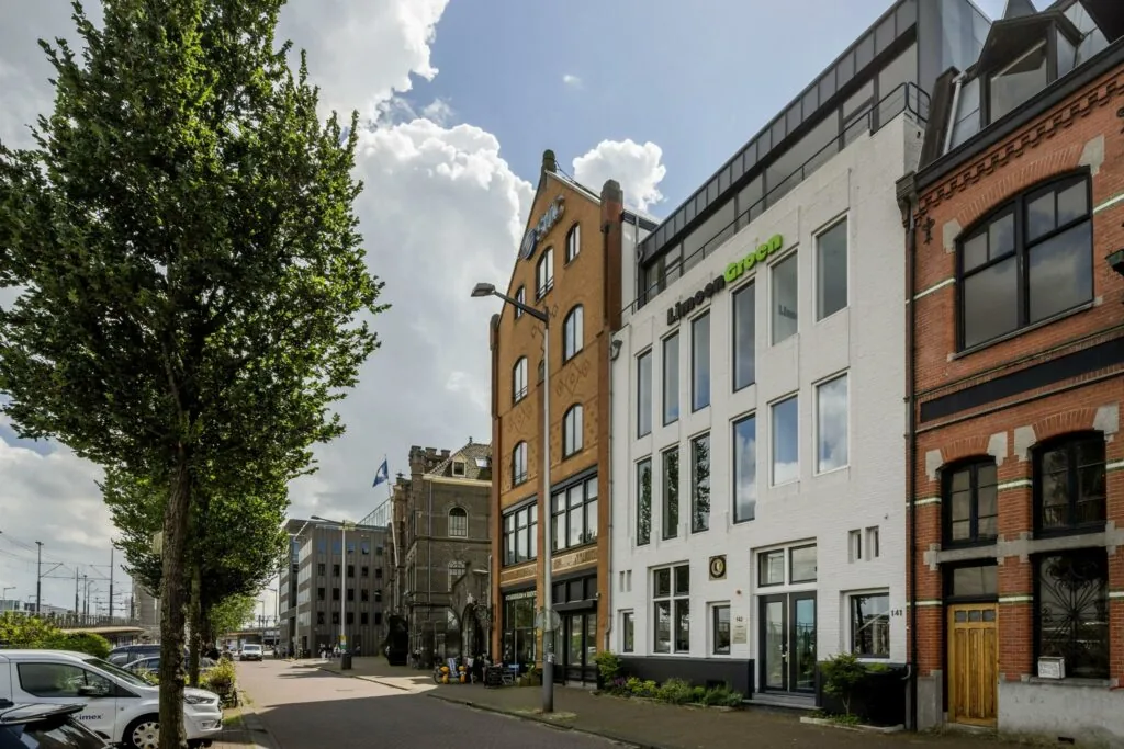 Gevels van verschillende kantoorpanden aan de De Ruijterkade in Amsterdam, met bomen en geparkeerde auto's op de voorgrond.